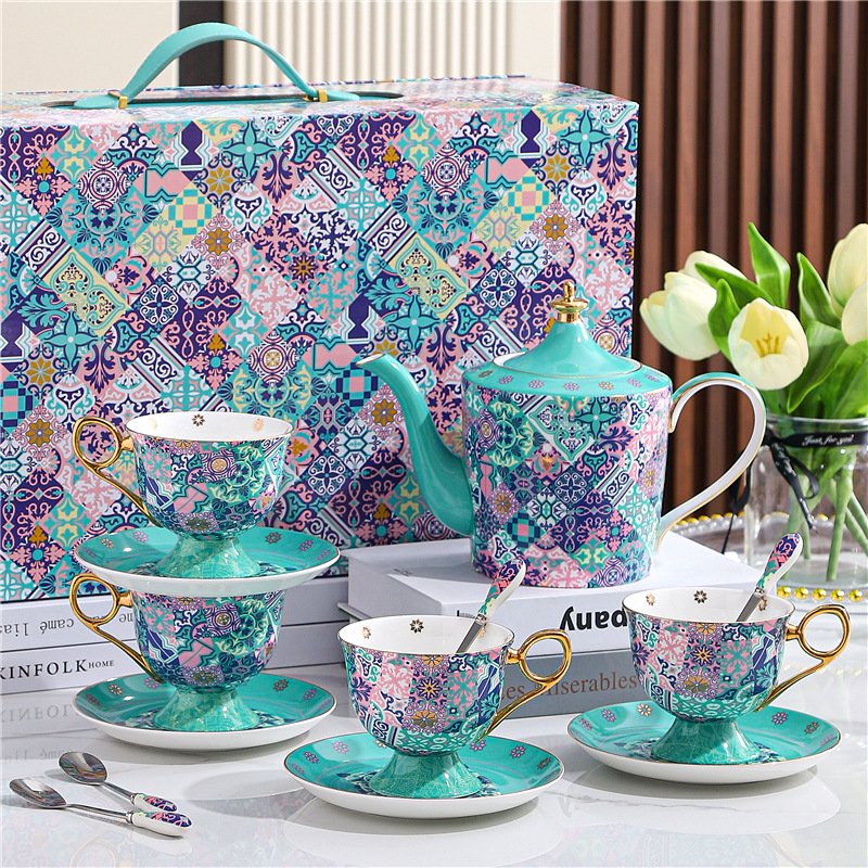 A luxury ceramic tea set arranged on a white surface, featuring a matching teapot, teacups with saucers, spoons, and a decorative gift box, all adorned with a vibrant turquoise and purple mosaic tile pattern