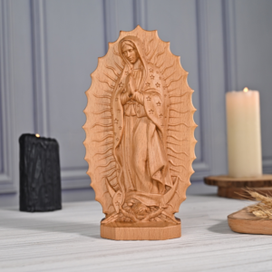 Standing handcarved wooden figurine of Our Lady of Guadalupe set within a radiant mandorla-shaped plaque with sunburst details, displayed on a wooden table between two candles