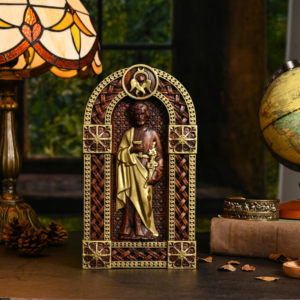 Ornate arced wooden-finish shrine plaque depicting Saint Joseph holding a staff with golden robes, framed by intricate Celtic lattice scrollwork on a desk alongside a stained glass lamp and vintage globe