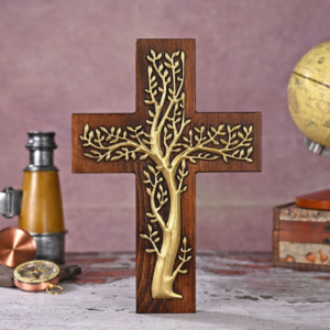 Dark walnut wooden cross featuring a gold-toned brass inlay of a flourishing Tree of Life with sprawling leafy branches set against a vintage desk background with a telescope, compass, and globe