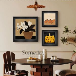 A dining room wall featuring a gallery set of three black-framed art prints: a large square print of white orchids in a pot on the left, and two smaller square prints stacked vertically on the right depicting small fruits and a textured yellow pumpkin