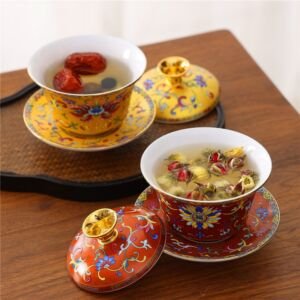 Two traditional Chinese porcelain gaiwan tea sets, one yellow and one red, featuring imperial enamel floral patterns with matching lids and saucers, filled with brewed herbal and flower tea on a wooden tabletop