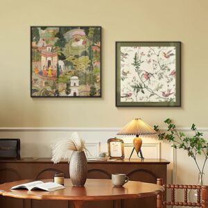 Two framed square art prints hanging side-by-side above a wooden console table; the left print features an intricate Indian Mughal garden scene with figures and architecture, while the right print displays delicate botanical branches with hummingbirds on a cream background