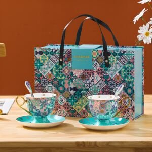 Two porcelain teacups and matching turquoise saucers featuring a colorful Mediterranean mosaic tile pattern, set in front of a matching gift box with black carrying straps