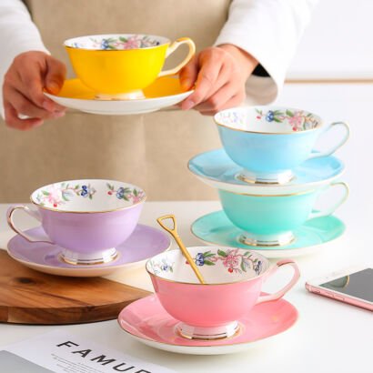 Assortment of vibrant pastel ceramic teacups and saucers in yellow, sky blue, mint green, lavender, and pink, each adorned with a gold rim and interior floral border print