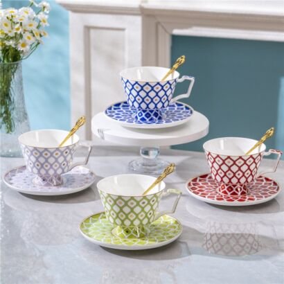 Four colorful porcelain teacups featuring a Moroccan trellis diamond pattern in blue, red, lime green, and lavender, each sitting on a matching saucer with a gold spoon