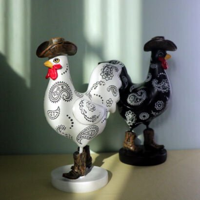 Two decorative rooster figurines wearing cowboy hats and western cowboy boots, featuring one white rooster with black paisley patterns and one black rooster with white paisley patterns