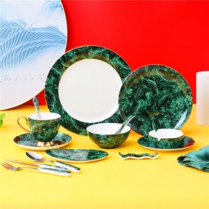A luxurious porcelain dinnerware set featuring rich malachite green marble patterns with gold accents, including plates, a tea cup and saucer, bowls, and cutlery arranged on a bright surface