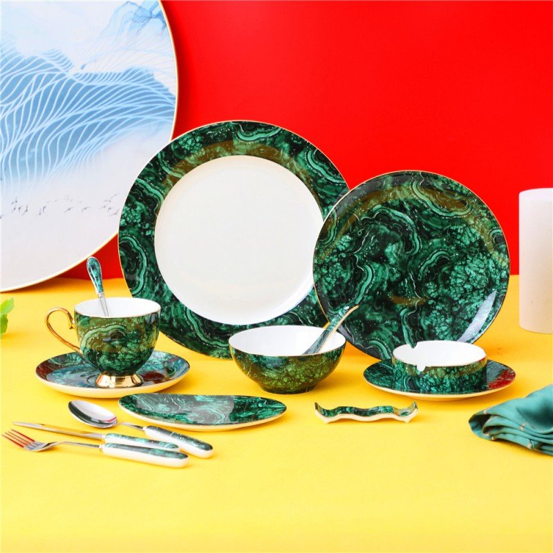 A luxurious porcelain dinnerware set featuring rich malachite green marble patterns with gold accents, including plates, a tea cup and saucer, bowls, and cutlery arranged on a bright surface