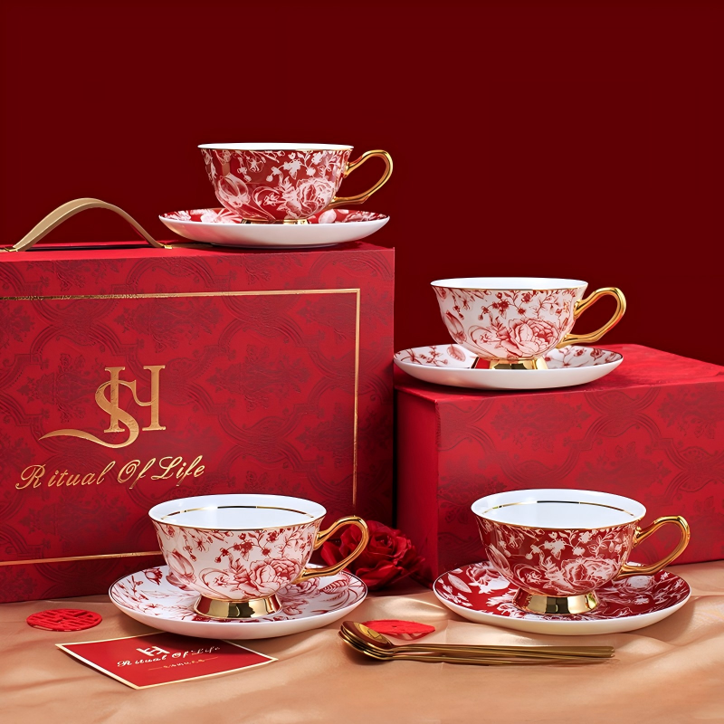 A luxury ceramic teacup and saucer set displayed alongside a red "Ritual of Life" gift box, featuring four teacups and matching saucers adorned with intricate red floral patterns and gold accents, accompanied by gold spoons