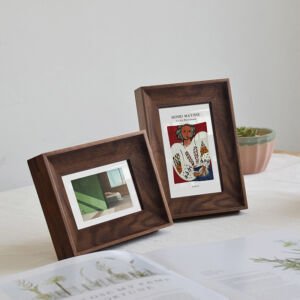 Two dark wooden picture frames resting on a white tabletop, featuring a horizontal frame with a minimalist interior view and a vertical frame displaying a Henri Matisse exhibition art print