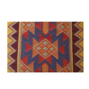 A close-up shot of a woven textile featuring a bold Southwestern geometric pattern with repeating diamonds, chevrons, and vertical zigzags in rich tones of red, blue, yellow, and orange