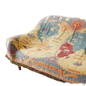 A sofa draped with a woven throw blanket featuring an antique world map design with continents, oceans, compass graphics, and an "Around the World" banner, finished with fringed edges