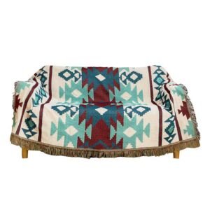 A sofa draped with a woven throw blanket featuring a bold Southwestern geometric pattern in turquoise, maroon, and cream, complete with textured fringe edges