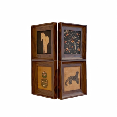 Four square deep-set walnut wood frames arranged in a 2x2 grid displaying folk-style art, including a light silhouette animal figure, a botanical bird print on black, dual ornamental vases, and a speckled big cat
