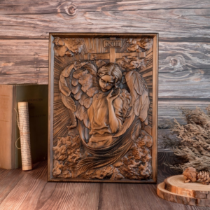 Ornately carved dark wood relief plaque featuring a winged guardian angel in prayer positioned in front of a cross with INRI inscription, set on a wooden table