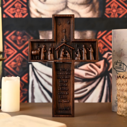 Carved dark wooden cross featuring a 3D Nativity scene across the arms and engraved Scripture text on the base
