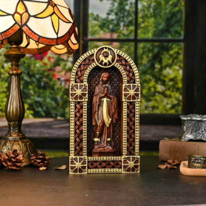 Ornately carved wooden arched shrine statue depicting the Virgin Mary in prayer with gold geometric lattice accents on a table