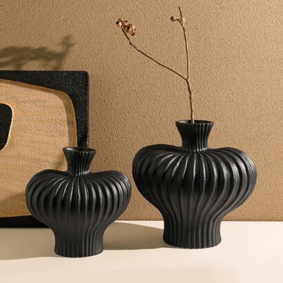 Pair of modern matte black fluted ceramic vases with distinct vertical ribbed textures sitting on a table with a dry botanical branch inside