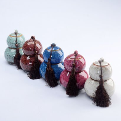Five small gourd-shaped ceramic tea storage caddies lined up diagonally in various crackle glaze colors—celadon green, amber brown, cobalt blue, magenta pink, and off-white—each adorned with a dark brown tassel.