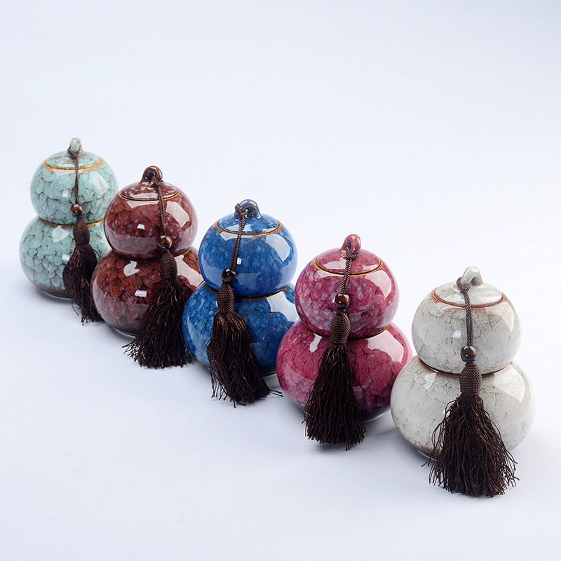 Five small gourd-shaped ceramic tea storage caddies lined up diagonally in various crackle glaze colors—celadon green, amber brown, cobalt blue, magenta pink, and off-white—each adorned with a dark brown tassel.