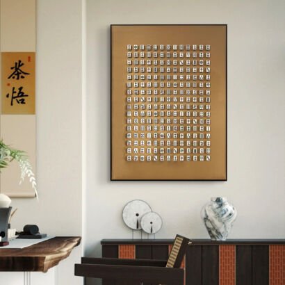 A large vertical black-framed 3D shadow box art piece displaying a full set of miniature white mahjong tiles arranged neatly in rows against a warm bronze gold background above a sideboard.