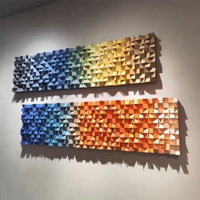 Two wide horizontal 3D wooden wall sculptures made of angled geometric wood blocks displaying colorful gradient shades from blue to yellow and orange mounted on a gray wall with dramatic directional lighting.
