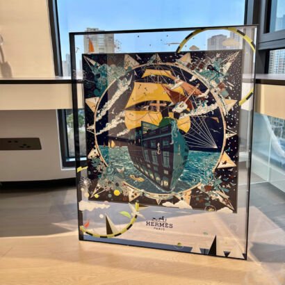A large square framed silk scarf art piece featuring a nautical sailing ship and compass design suspended inside a transparent acrylic frame with black borders.