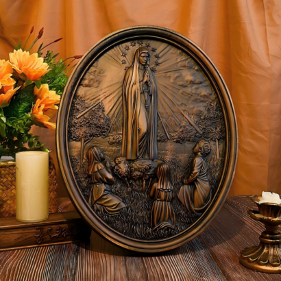 An oval wall plaque featuring a detailed high-relief carving with an antique bronze-toned finish, depicting Our Lady of Fatima standing surrounded by radiant light rays and a halo of stars above three kneeling shepherd children, displayed on a wooden surface next to yellow flowers and a candle holder.