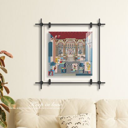 A colorful surrealist architectural artwork mounted inside a floating acrylic glass frame with a black geometric metal border on a warm beige living room wall.