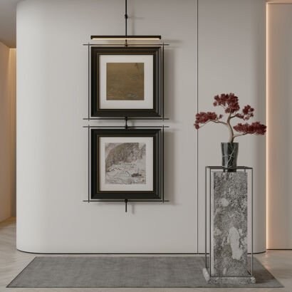 Two vertically stacked framed Asian landscape artworks hanging from a black metal rod with an integrated picture light next to a potted red bonsai tree on a marble pedestal.