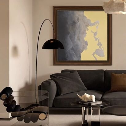Modern living room interior featuring a dark grey sofa, a sleek black arc floor lamp, and a large framed abstract canvas artwork in grey and yellow tones.