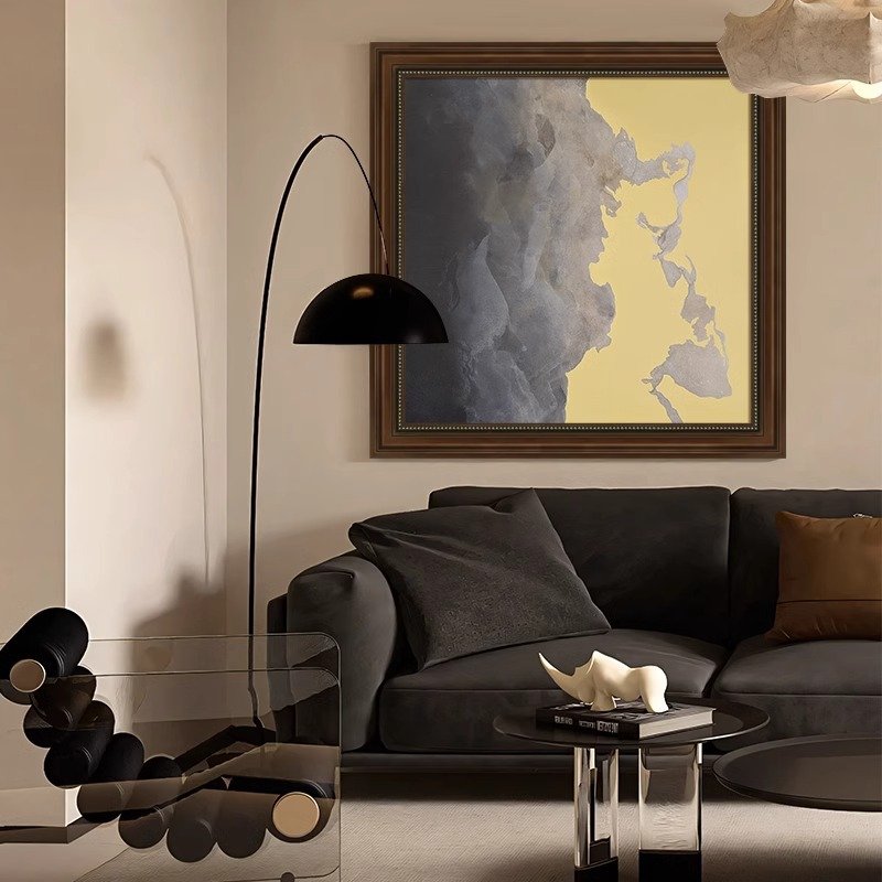 Modern living room interior featuring a dark grey sofa, a sleek black arc floor lamp, and a large framed abstract canvas artwork in grey and yellow tones.