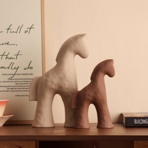 Pair of minimalist abstract ceramic horse sculptures in textured beige and warm terracotta clay standing on a wooden table alongside books and framed wall art