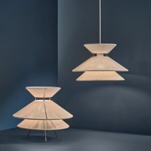A modern architectural lighting collection featuring a hanging pendant light and matching table lamp, both crafted with cream-white woven cord wrapped around a three-tiered conical geometric metal frame against a moody dark blue background.