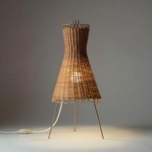 A vintage-style woven rattan table lamp featuring an hourglass silhouette shade with scalloped looped edges supported by sleek brass tripod metal legs, isolated on a grey background.