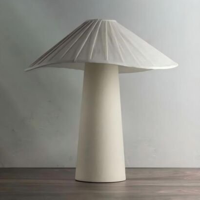 A modern off-white ceramic table lamp featuring a tapered conical base and a wide pleated umbrella-shaped mushroom shade on a wooden surface against a neutral background.