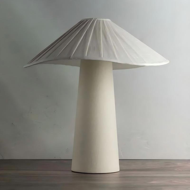 A modern off-white ceramic table lamp featuring a tapered conical base and a wide pleated umbrella-shaped mushroom shade on a wooden surface against a neutral background.