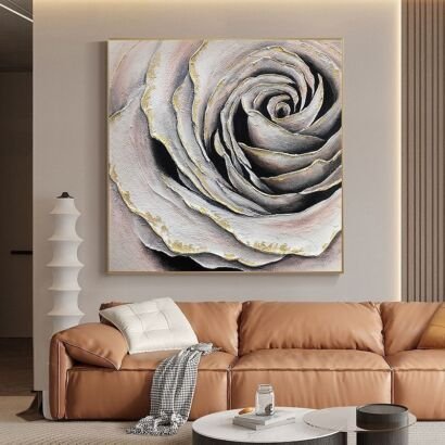 A large square 3D textured canvas painting depicting a dramatic close-up spiral of rose petals in grey, blush, and white with metallic gold foil edges, displayed above a tan leather couch in a modern living room.