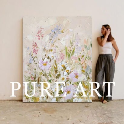 A large vertical textured abstract canvas painting depicting a meadow of delicate wildflowers in soft lavender, pink, white, and sage green with thick impasto strokes on a beige background, displayed next to a woman standing by a neutral wall.