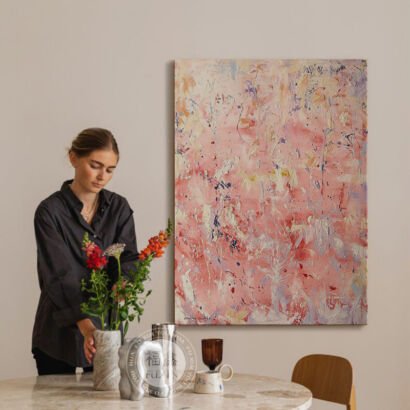 A large vertical textured abstract canvas painting featuring expressive impasto brushstrokes in soft pink, blush, white, and subtle lilac tones, displayed on a wall in a bright dining room.