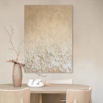 A large vertical heavily textured abstract canvas painting featuring neutral cream, sand beige, and plaster impasto textures mounted on a beige wall above a wooden dining table
