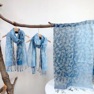 Three lightweight blue scarves with white floral leaf patterns displayed on wooden hangers and draped over a branch, featuring frayed fringe trim along the edges against a white backdrop.