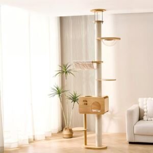 A tall, floor-to-ceiling wooden cat tree tower featuring a full sisal scratching post pole, a wooden cat condo, a clear acrylic space capsule bowl, a fabric hammock, and multiple stepping platforms in a bright, modern living room next to a potted palm plant and couch.