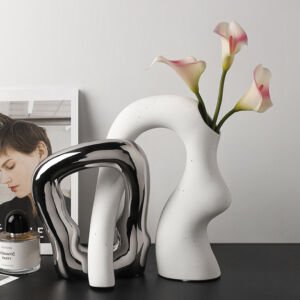 Modern interlocking abstract ceramic vases in liquid chrome silver finish and speckled matte white holding calla lilies on a tabletop