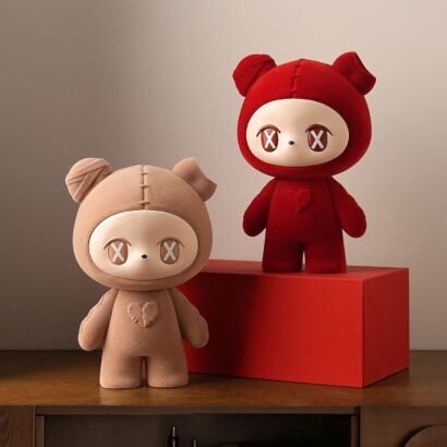 Two designer bear figurines in beige and bold red with 'X' eyes and stitching details sitting on a wooden cabinet next to a red riser box