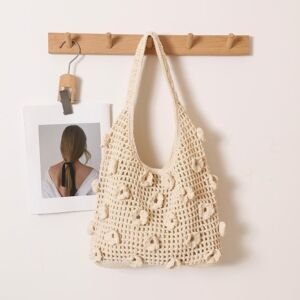 A cream-white handwoven crochet shoulder tote bag with 3D popcorn-stitch floral embellishments scattered across an open-work mesh knit, hanging on a wooden wall rack.