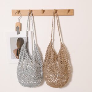 Two glittery crochet open-work straw hobo bags—one in metallic silver and one in metallic gold—hanging side-by-side on a wooden wall peg, featuring long matching woven shoulder straps.