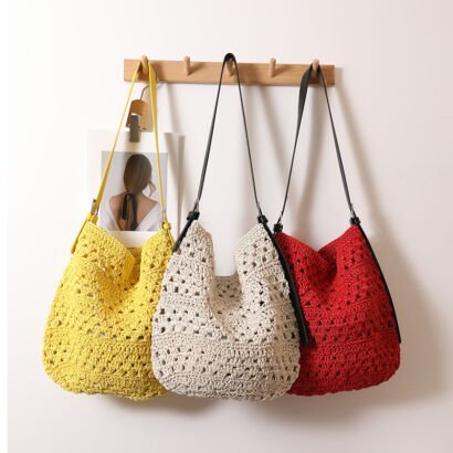 Three colorful handwoven crochet straw hobo tote bags in yellow, beige, and red hanging side-by-side on a wooden wall rack, each featuring contrast shoulder straps and a relaxed Slouchy design.
