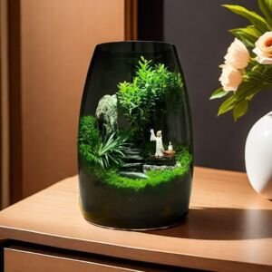 A curved smoky tinted glass terrarium jar on a warm wooden tabletop, featuring a lush green landscape with miniature foliage, moss, a natural rock pillar, and a tiny traditional scholar figurine.